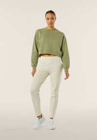 Sudadera recortada en color verde oliva con dobladillo acanalado, combinada con pantalones crema con costuras laterales y zapatillas blancas. Un aspecto simple y moderno.