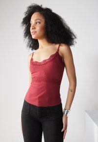 Burgunderfarget ribbestrikket tanktop med blonder langs halsen og midten, med tynne justerbare stropper og en tettsittende silhuett.