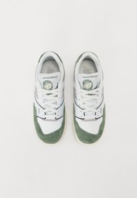 Baltos raišteliais avalynės batai su žaliais veliūro akcentais, turintys tekstūruotą dizainą, paminkštintą apykaklę ir apvalų logotipą ant liežuvio.