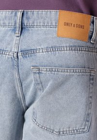 Jeans in denim azzurro chiaro con un taglio classico, dotati di tasche posteriori e un'etichetta in pelle marrone con la scritta "ONLY & SONS". Tessuto testurizzato con cuciture visibili.