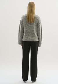 Grå stickad tröja med en strukturerad finish, med breda ärmar och en figursydd nederkant, i kombination med svarta byxor med vida ben.