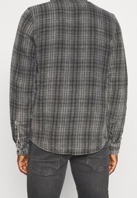 Kariertes Flanellhemd in Grautönen mit langen Ärmeln, geknöpften Manschetten, abgerundetem Saum und lockerem Sitz. Das Gewebe hat eine weiche Textur.