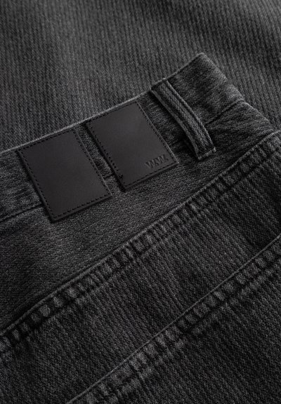 Fekete farmer texturált anyaggal, dupla fekete bőr címkével az deréknál és kontrasztos varrással.