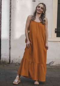 Roestkleurige maxi-jurk met een gestructureerd oppervlak, voorzien van een uitlopende onderkant en dunne bandjes. G gedragen met lichte platform sandalen.