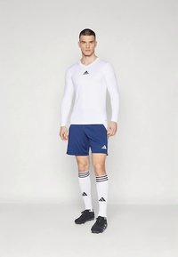 Valge pika varrukaga spordipusa ümara kaelusega, ühendatud meresiniste lühikeste pükstega, valgete sokkidega, millel on mustad triibud, ja mustade jalgpallijalatsitega.