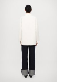 White quilted jacket with long sleeves, paired with dark navy wide-leg jeans featuring contrasting denim cuffs. Simple, minimalist design.