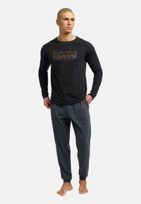 Sort langærmet skjorte med grafisk tekst, parret med grå joggebukser med diskret broderi. Stoffet er blødt og har en afslappet pasform.