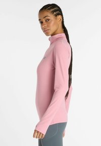 Langärmliges, hochgeschlossenes Oberteil in Hellrosa, aus einem glatten, dehnbaren Material. Verfügt über ein dezentes Logo auf der Brust und eine taillierte Passform.