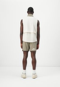 Sleeveless white top layered over an olive green shirt, paired with olive shorts. Light sneakers with white socks. Plain background.