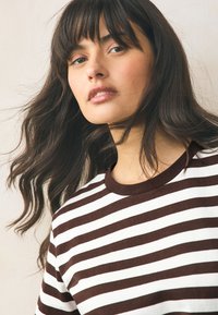 Barna-fehér csíkos póló kerek nyakkivágással, puha anyagból készült, kényelmes szabással és rövid ujjakkal.