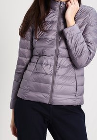 Jasnofioletowa kurtka puchowa z poziomym pikowaniem, wysokim kołnierzem i zapięciem na zamek z przodu. Materiał wiatroszczelny i dopasowany krój.