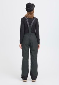 Svart langermet topp kombinert med mørkegrønne snøbukser med seler, elastisk midje og forsterkede benåpninger.