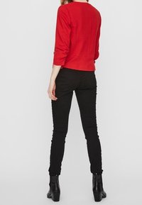 Red ribbed long-sleeve top with a round neckline, paired with black skinny pants and ankle boots. Focus on fit and simplicity in design.