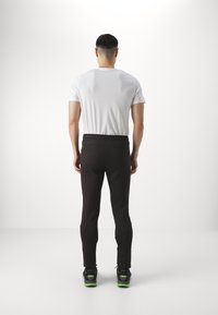 Zwarte, aansluitende sportbroek met een zachte textuur, elastische tailleband en ritsaccenten; gecombineerd met een wit T-shirt met korte mouwen en zwarte sneakers.