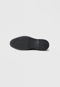 Suola di scarpa in gomma nera con un motivo testurizzato, forma arrotondata e branding sottile. Transizione fluida dal tallone alla punta.