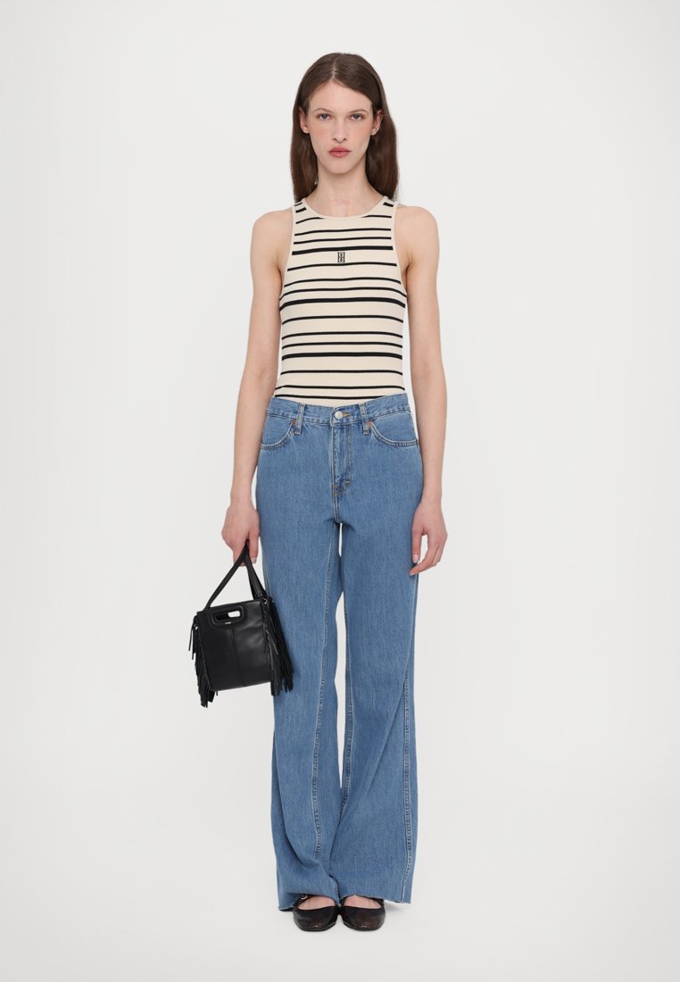Top à rayures en crème et noir, jeans bleus taille haute, sac noir à franges et ballerines noires. Tenue simple et décontractée.