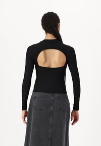 Black long-sleeve top with a round cutout at the back, fitted design, and soft texture. Paired with a dark gray denim skirt featuring pockets.