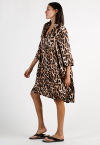 Leopardenmuster-Kleid aus leichtem Stoff, mit V-Ausschnitt, 3/4-Ärmeln und einer lockeren, fließenden Silhouette. Kombiniert mit schwarzen Flip-Flops.
