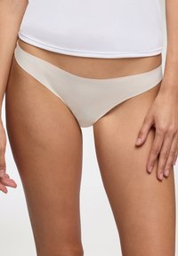 Perizoma beige con una finitura liscia e semi-opaca, dotato di una cintura sottile e un design a copertura minima.