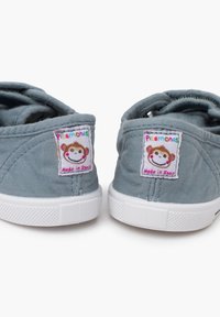 Chaussures en toile grises claires avec semelles blanches, ornées de patchs colorés représentant des singes et étiquetés "Pisamonas" et "Fabriqué en Espagne."