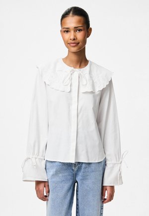 White blouse featuring a large embroidered collar, tie detail at the neck, and elasticized cuffs with drawstring. Worn with light blue jeans.