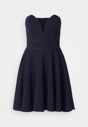 Vestido azul marino sin tirantes con un escote en forma de corazón, cuerpo ajustado y falda acampanada. Presenta un detalle de cinturilla con borde festoneado. Confeccionado en una tela suave.