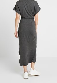 Graues Maxikleid aus Jersey mit kurzen Ärmeln, taillierter Taille, seitlichen Schlitzen und lockerer Passform, getragen mit weißen Sneakers. Einfaches, lässiges Design.