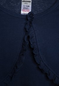 Indumento blu navy a maniche corte con scollo rotondo e rifinitura a ruffle. Include una piccola chiusura con bottone. Etichetta di cura mostrata all'interno.