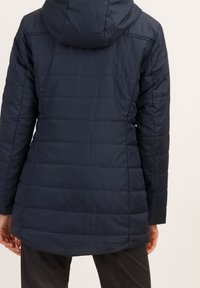 Mörkblå dunjacka med huva, med vertikal quiltning, långa ärmar och en något utsvängd nederkant, tillverkad av vattenavvisande material.