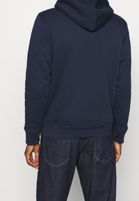 Námořnicky modrá mikina s kapucí a texturovaným povrchem, s kapucí, žebrovanými manžetami a lemem, doplněná tmavě modrými džínami.