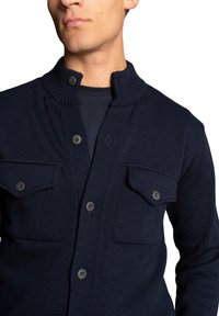 Dark navy knitted cardigan featuring a high collar, buttoned closure, and two chest pockets with flat flaps and buttons.