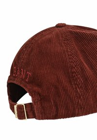 Braune Cordmütze mit strukturierter Oberfläche, besticktem Logo auf der Rückseite und einem verstellbaren Metallriemen mit rechteckiger Schnalle.