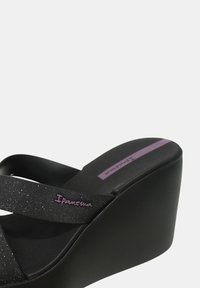 Sandalo wedge nero con una texture liscia, dotato di cinturini incrociati scintillanti e un logo viola. Design sottile nella parte superiore con una soletta imbottita.