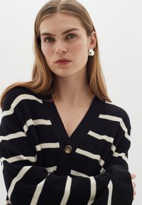 Marinrandig cardigan med vita horisontella ränder, V-hals och en knäppning med en knapp. Mjuk stickad textur med vida ärmar.