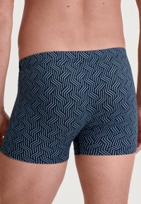 Marineblauwe boxershorts met een geometrisch wit patroon. Het materiaal is zacht met een gladde textuur. De tailleband is elastisch en sluit strak aan.
