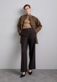 Bruine houndstooth oversized jas over een tan top, gecombineerd met hoge zwarte wijde broek en zwarte puntige hakken. Gladde texturen.