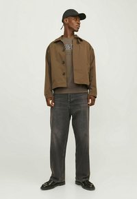 Pruun lühendatud jakk mustade nööpidega, hall t-särk all, laiad hallid teksad ja mustad kingad. Aksessuaaridena on must müts.