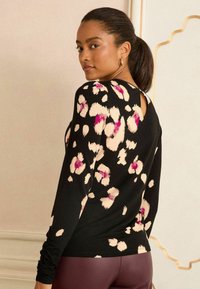 Hosszú ujjú fekete felső, élénk pink és krém színű leopardmintával. Egyszerű, kerek nyakú, hátul kis kulcslyuk részlettel.