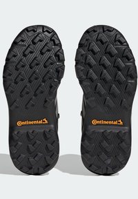 Suela de calzado negra con un patrón de dibujo robusto que presenta formas parecidas a flechas. Logotipo "Continental" en naranja cerca del talón.