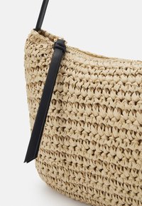 Tkaná slaměná taška béžové barvy s texturovaným povrchem. Disponuje černým koženým popruhem a zapínáním na zip. Kompaktní, zakřivený design.