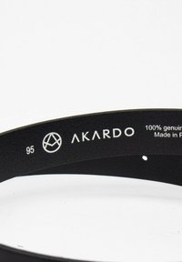 Zwarte leren riem met een gladde textuur. Bevat de merknaam "AKARDO" en maatinformatie. Gemaakt van 100% echt leer.