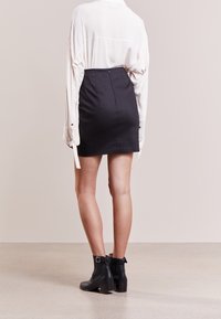 Falda negra ajustada con cremallera en la parte posterior, combinada con una camisa blanca holgada de botones. Botines negros con detalle de hebilla completan el look.