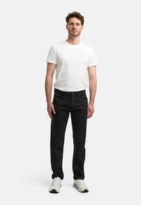 Jeans de mezclilla negros de corte recto, combinados con una camiseta ajustada de algodón blanca. El modelo lleva zapatillas grises y blancas.