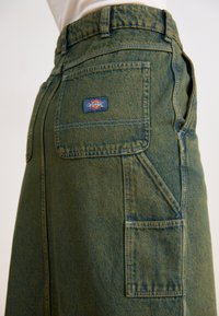 Vihreä denimhame, jossa on korkea vyötärö ja sivutaskut. Varustettu näkyvällä logopatilla ja teksturoidulla kankaalla, jossa on haalistunut viimeistely.