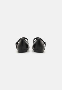 Zapatos de cuero negro mate con punta redondeada y correa en el tobillo. Textura suave y diseño minimalista, con acentos cosidos.