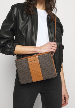 Borsa marrone con logo stampato e dettagli borchiati, caratterizzata da una striscia in pelle beige. Tracolla a catena; forma rettangolare, texture liscia e chiusura a zip.