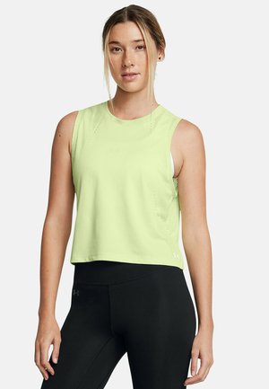 Donna con capelli biondi che indossa un top atletico senza maniche di colore verde chiaro e leggings neri, in piedi su uno sfondo bianco uniforme.