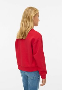 Sweat-shirt rouge à col rond avec des manches longues et des poignets côtelés. Vue de dos, porté avec un jean bleu clair, en matière de coton lisse.