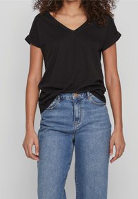 Černé tričko s V výstřihem a ohrnutými krátkými rukávy, v kombinaci s džíny z lehkého modrého denimu s vysokým pasem. Měkká tkanina; volný střih.