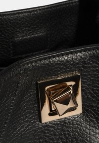 Zwart gestructureerd leer met een glanzende afwerking, voorzien van een vierkant gouden metalen sluiting met een geometrisch ontwerp.